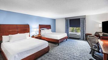 A hotel room with two beds, a desk, a chair, a TV, and a window with curtains.