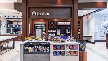A coffee shop with a sign reading "The Shop" and a display of fresh-brewed coffee, tea, latte, cappuccino, and specialty coffee available all day.