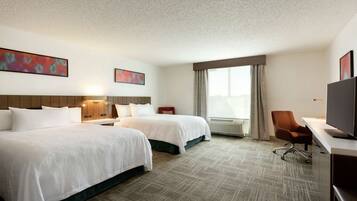 A hotel room with two beds, a desk, a chair, and a television.