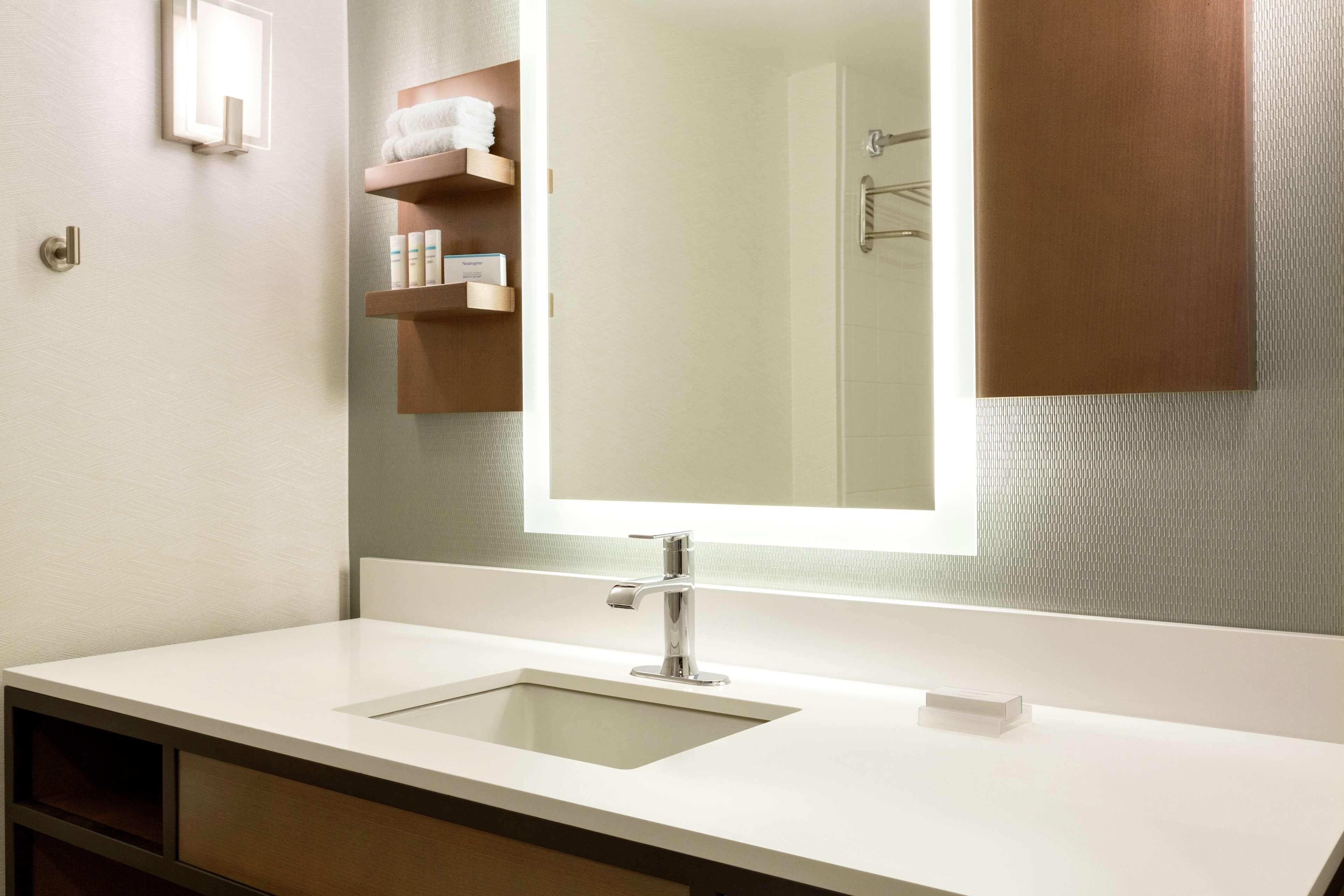 Un baño moderno con un lavabo blanco, un espejo grande y un perchero para toallas.