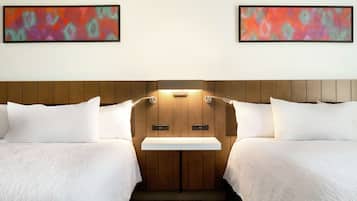 Une chambre d’hôtel avec deux lits, une tête de lit en bois, une petite table de chevet et deux tableaux abstraits accrochés au mur.