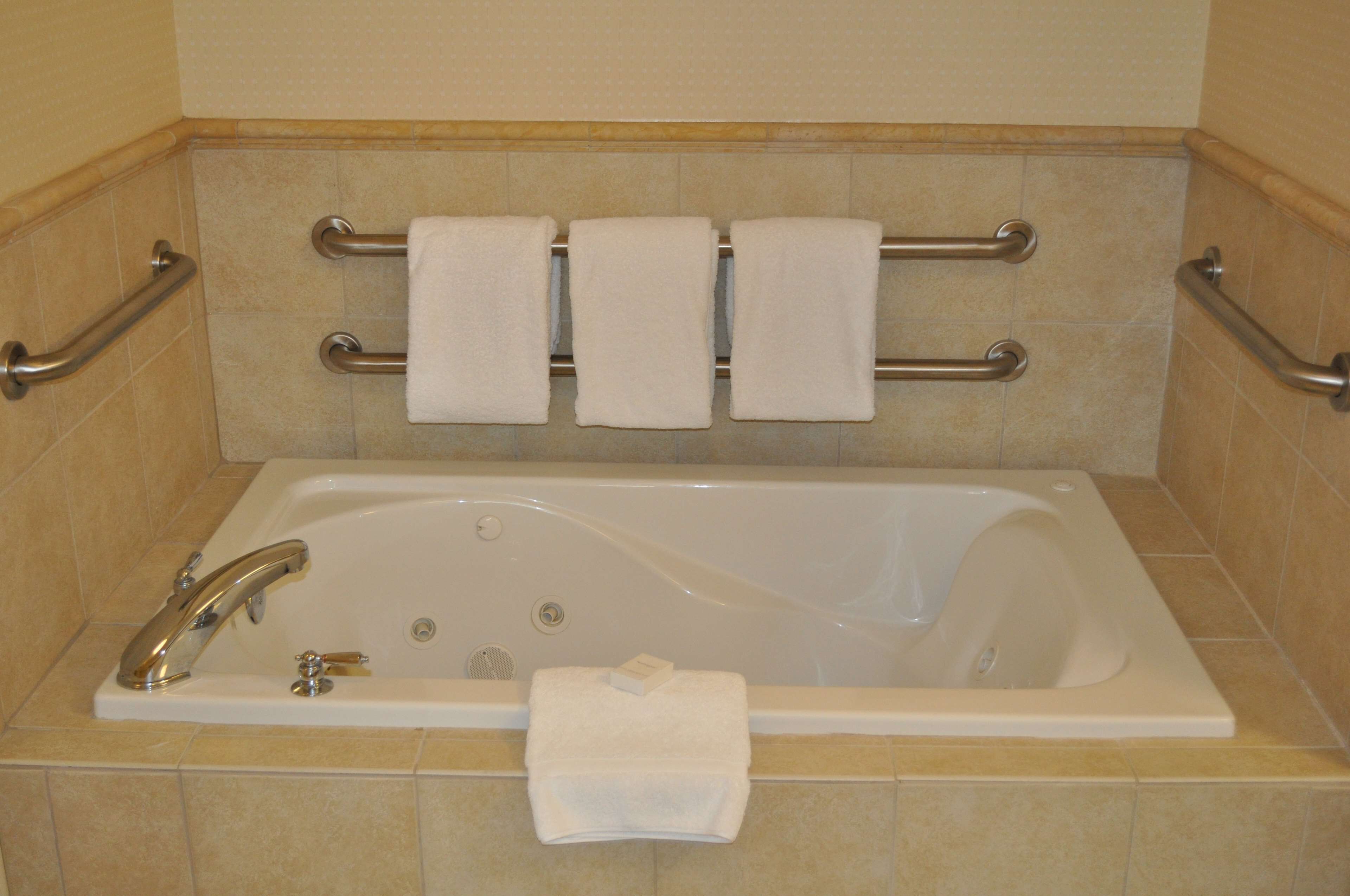 Un baño con bañera, barras de apoyo y tres toallas.