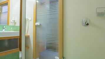 A bathroom with a glass door, a green-tiled floor, a white sink, and a mirror.