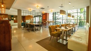 A modern hotel lobby with a reception desk, seating areas, and large windows offering natural light and views. - Impiq Hotel (Trnava)
