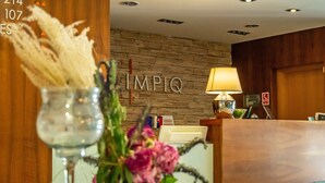 A reception desk with a wooden wall, a lamp, and a vase with flowers. - Impiq Hotel (Trnava)