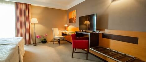 Une chambre d’hôtel avec un lit, un bureau, une chaise, une lampe et une œuvre d’art au mur.