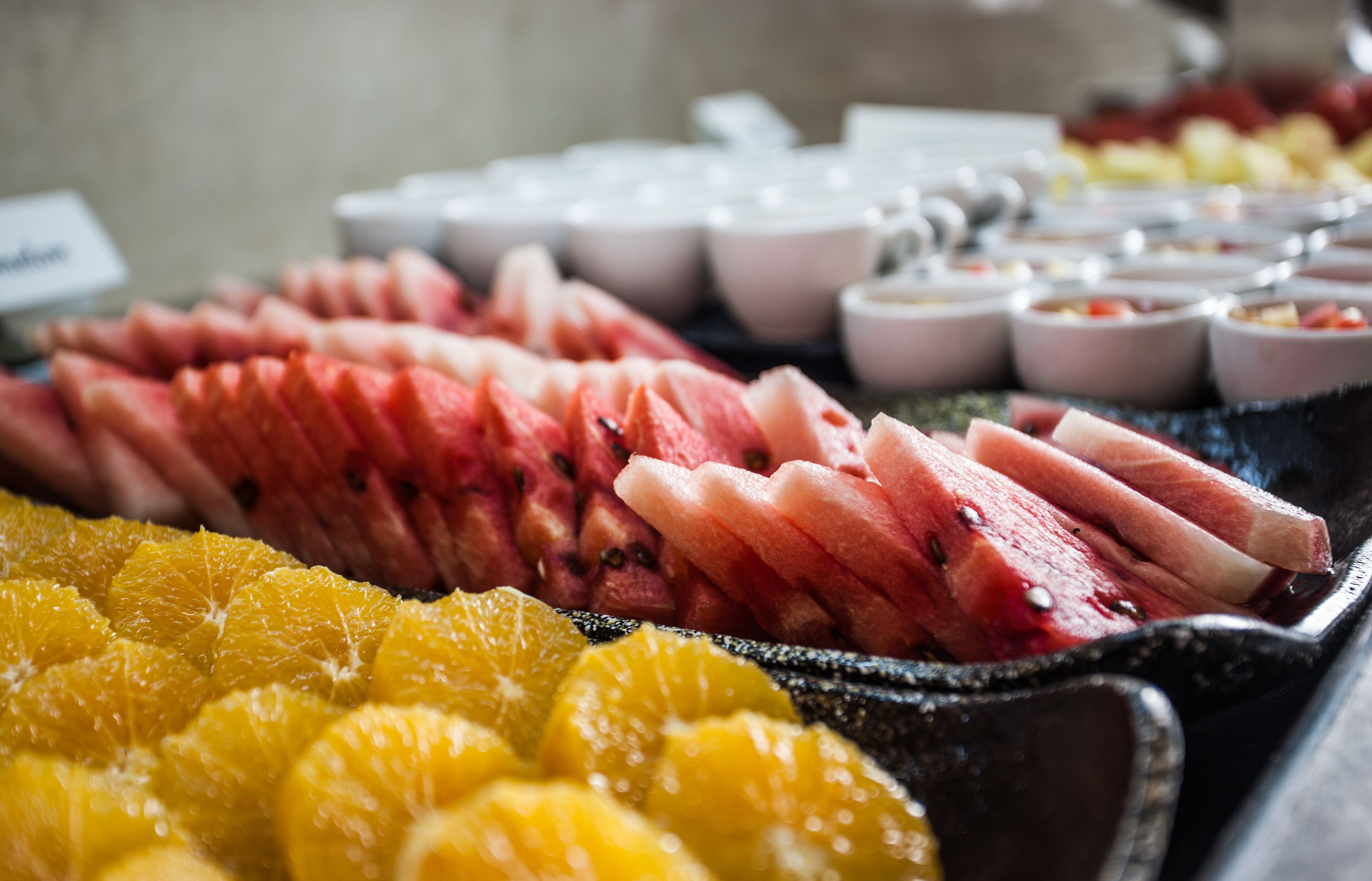 A buffet with sliced watermelon, oranges, and various fruit cups.