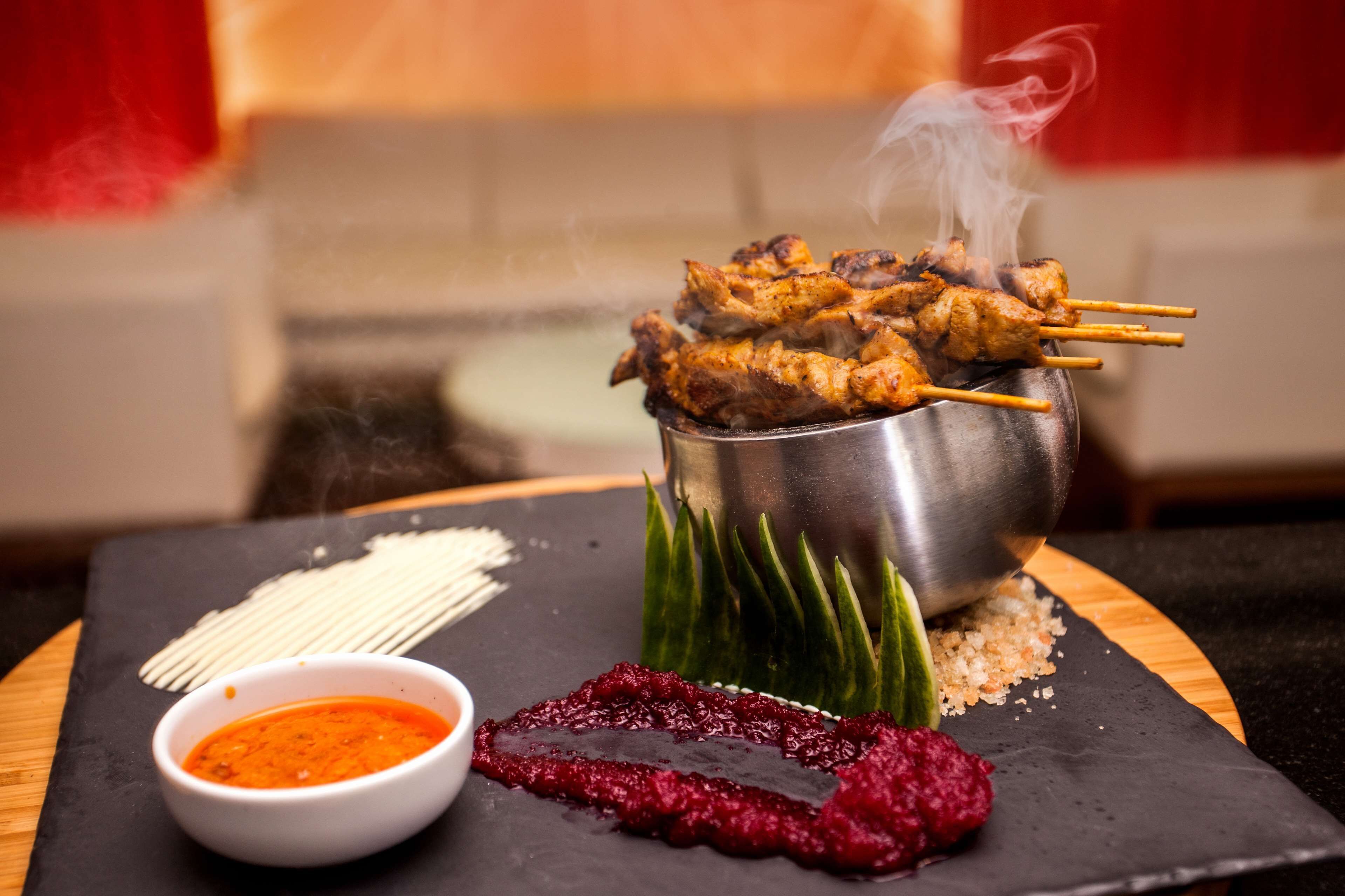 A dish of grilled skewers with a dipping sauce and a side of chutney on a slate plate.
