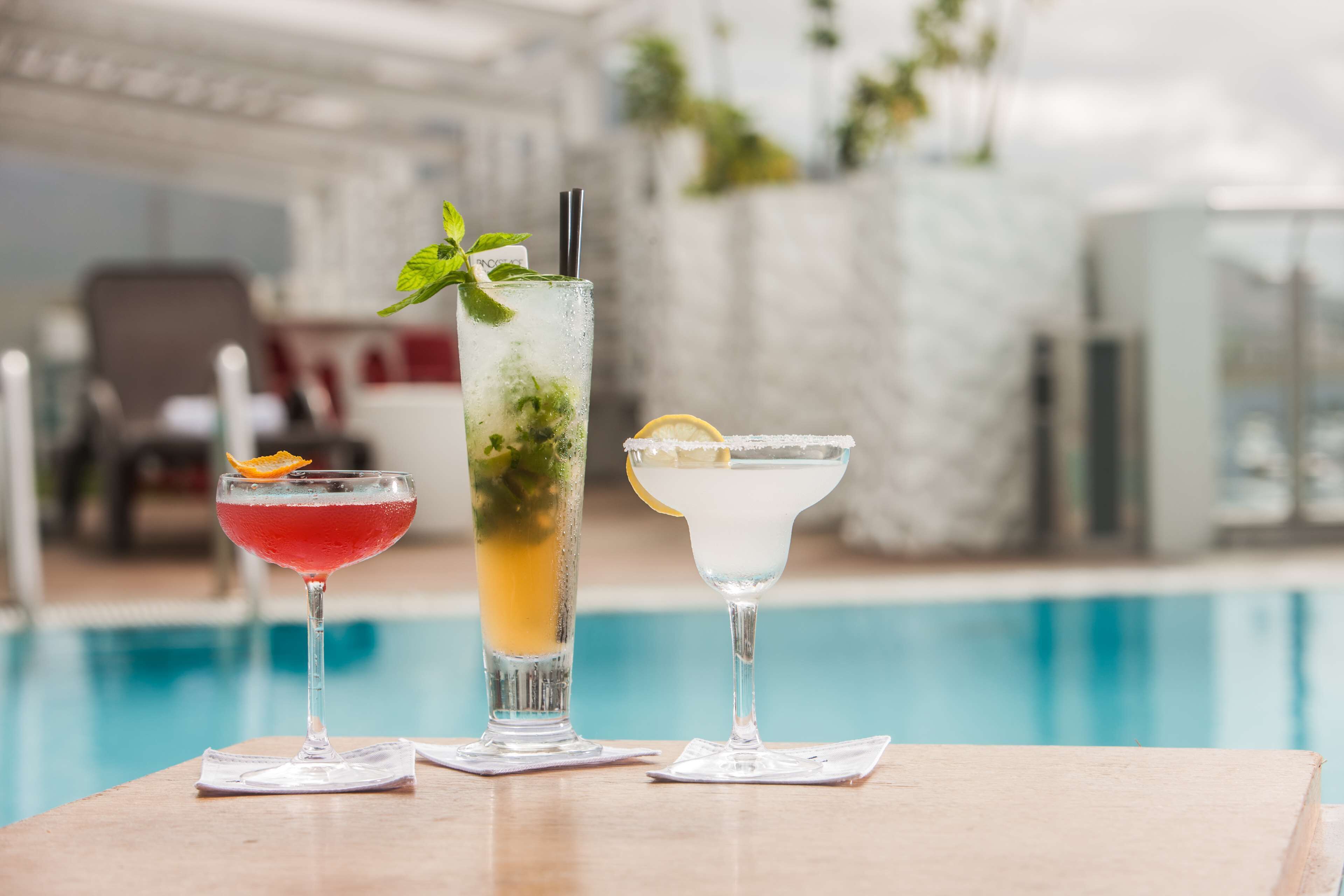 Three cocktails on a table by a poolside.