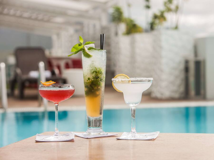 Three cocktails on a table by a poolside.