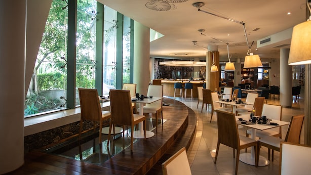 A modern restaurant with a curved seating area, large windows, and a bar in the background. - Hennessy Park Hotel (Ebene)