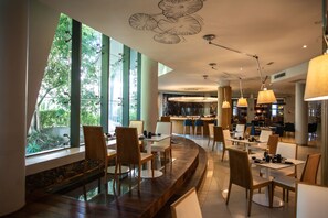 A modern restaurant with a curved seating area, large windows, and a bar in the background. - Hennessy Park Hotel (Ebene)