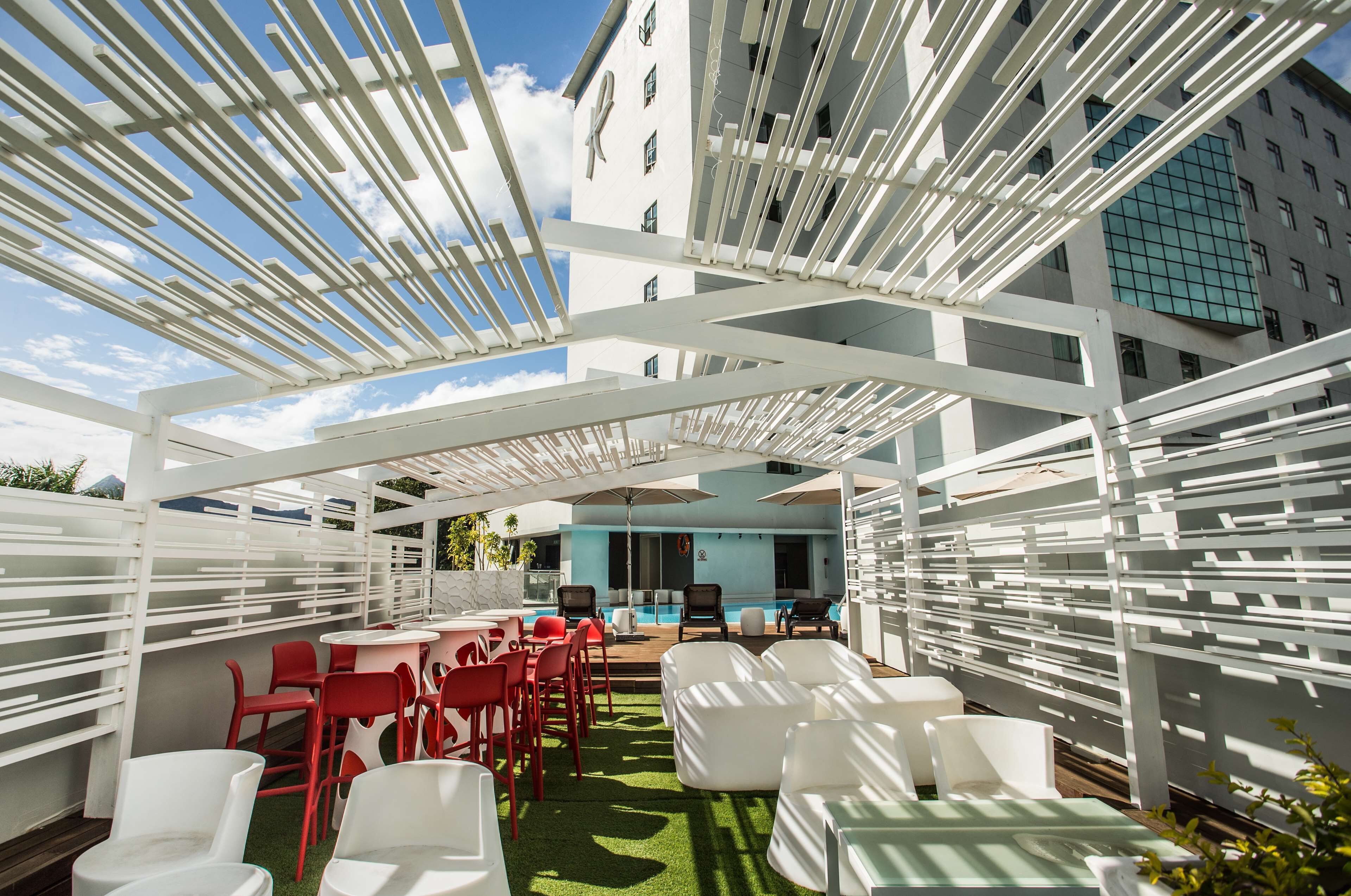 Een terras buiten met witte en rode stoelen, een zwembad en uitzicht op een gebouw met een blauwe gevel.
