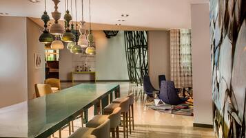 A modern dining area with a long table, multiple chairs, hanging pendant lights, and a contemporary art piece on the wall.