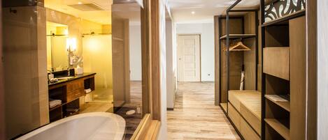 A modern bathroom with a freestanding bathtub, a vanity with a mirror, and a wooden shelving unit with a hanging garment rack.