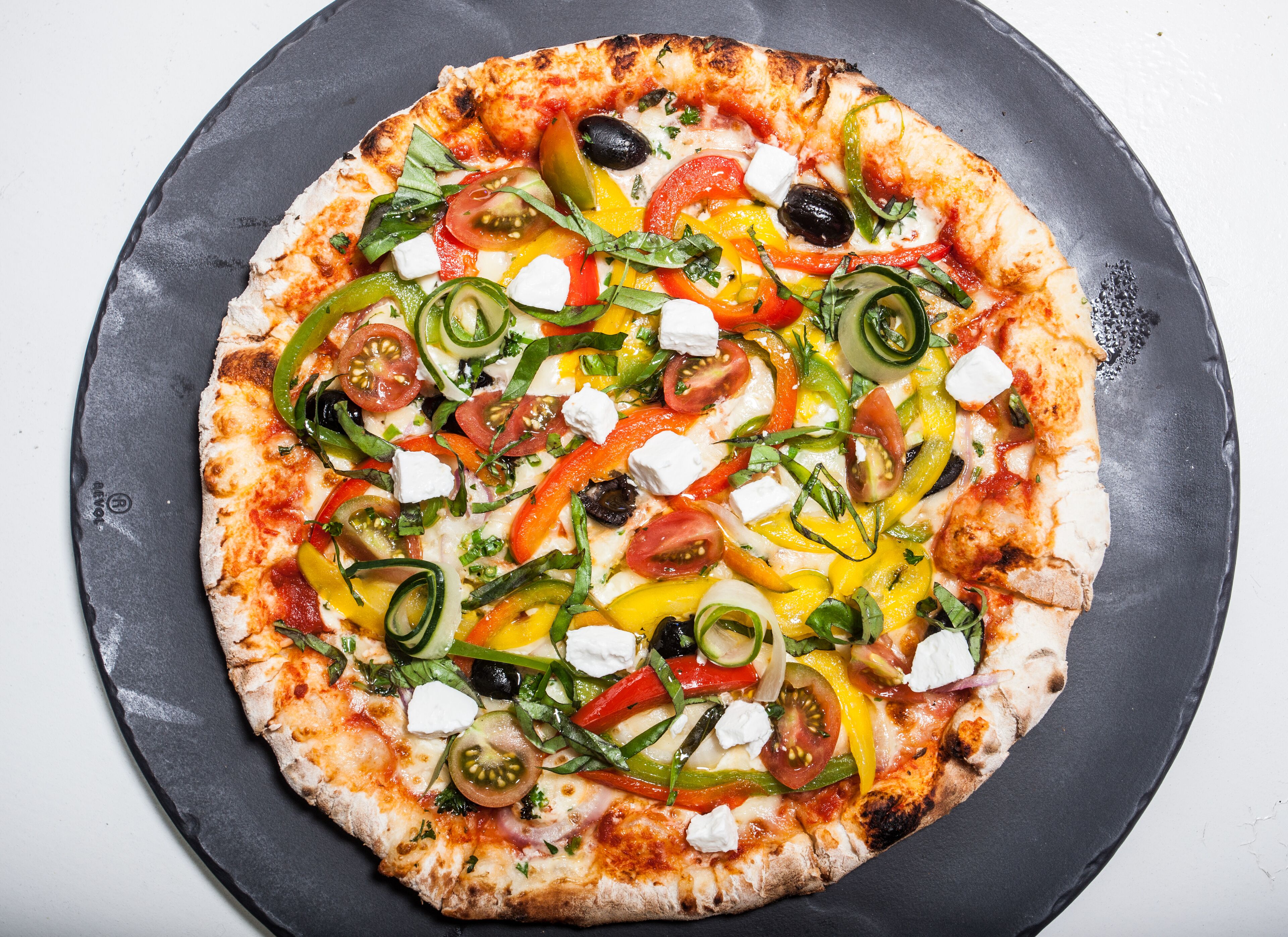 Una pizza con diversos ingredientes sobre un plato negro.