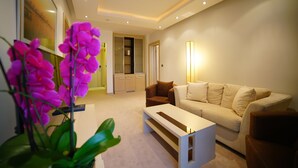 A modern living room with a beige sofa, a white coffee table, and a large window with a view of the outdoors. - Hotel Vojvodina (Zrenjanin)