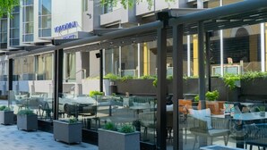 An outdoor seating area with tables and chairs, a glass enclosure, and a building with a sign that reads "VOJODINA HOTEL". - Hotel Vojvodina (Zrenjanin)