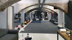 A gym with brick arches, exercise equipment, and a water bottle on a table. - Hotel Vojvodina (Zrenjanin)