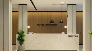 A modern hotel reception area with a marble counter, reception desk, and a potted plant. - Hotel Vojvodina (Zrenjanin)