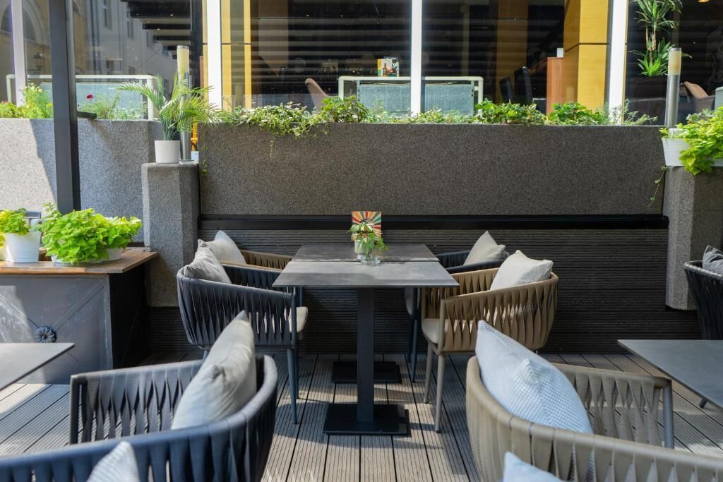 Un área de estar al aire libre con una mesa y sillas, rodeada de follaje y un diseño arquitectónico moderno.