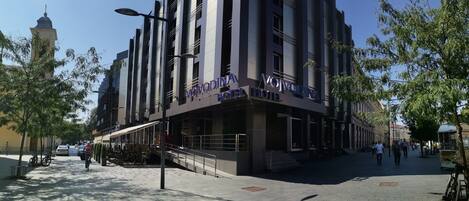 A modern hotel with a prominent sign, outdoor seating, and a pedestrian area.