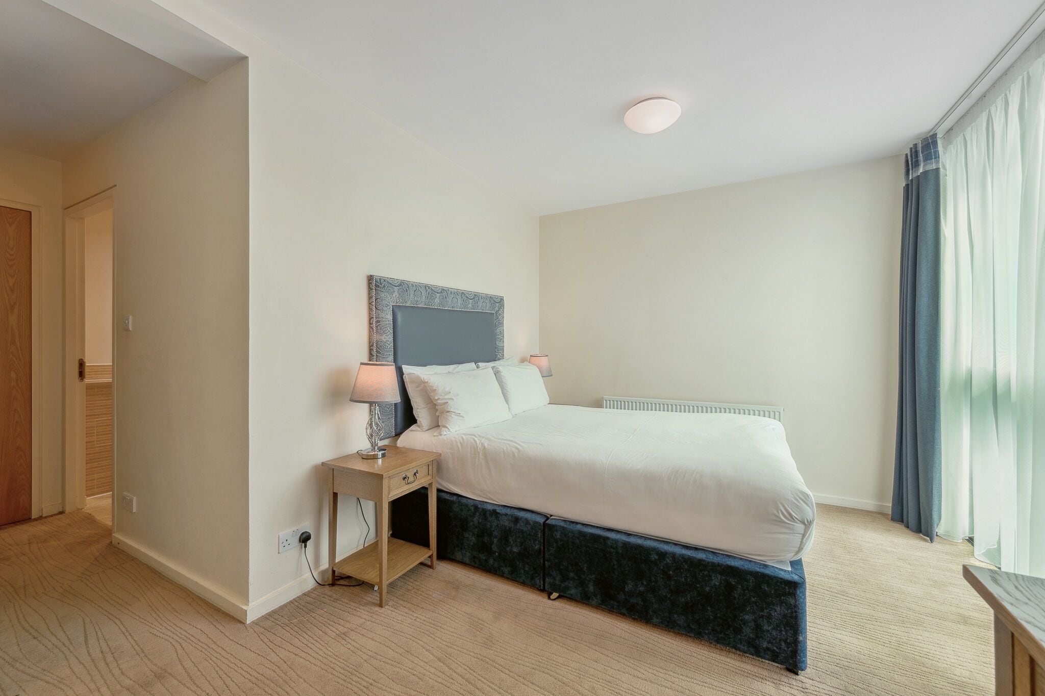 Een moderne slaapkamer met een bed, nachtkastje en een bijzetmeubel.