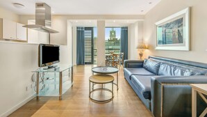 A modern living room with a blue sofa, a glass coffee table, and a TV on a glass cabinet. - Princes Street Suites (Edinburgh)