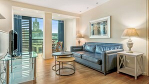 A modern living room with a leather sofa, a glass coffee table, and a white side table. A large window offers a view of a historic clock tower. - Princes Street Suites (Edinburgh)