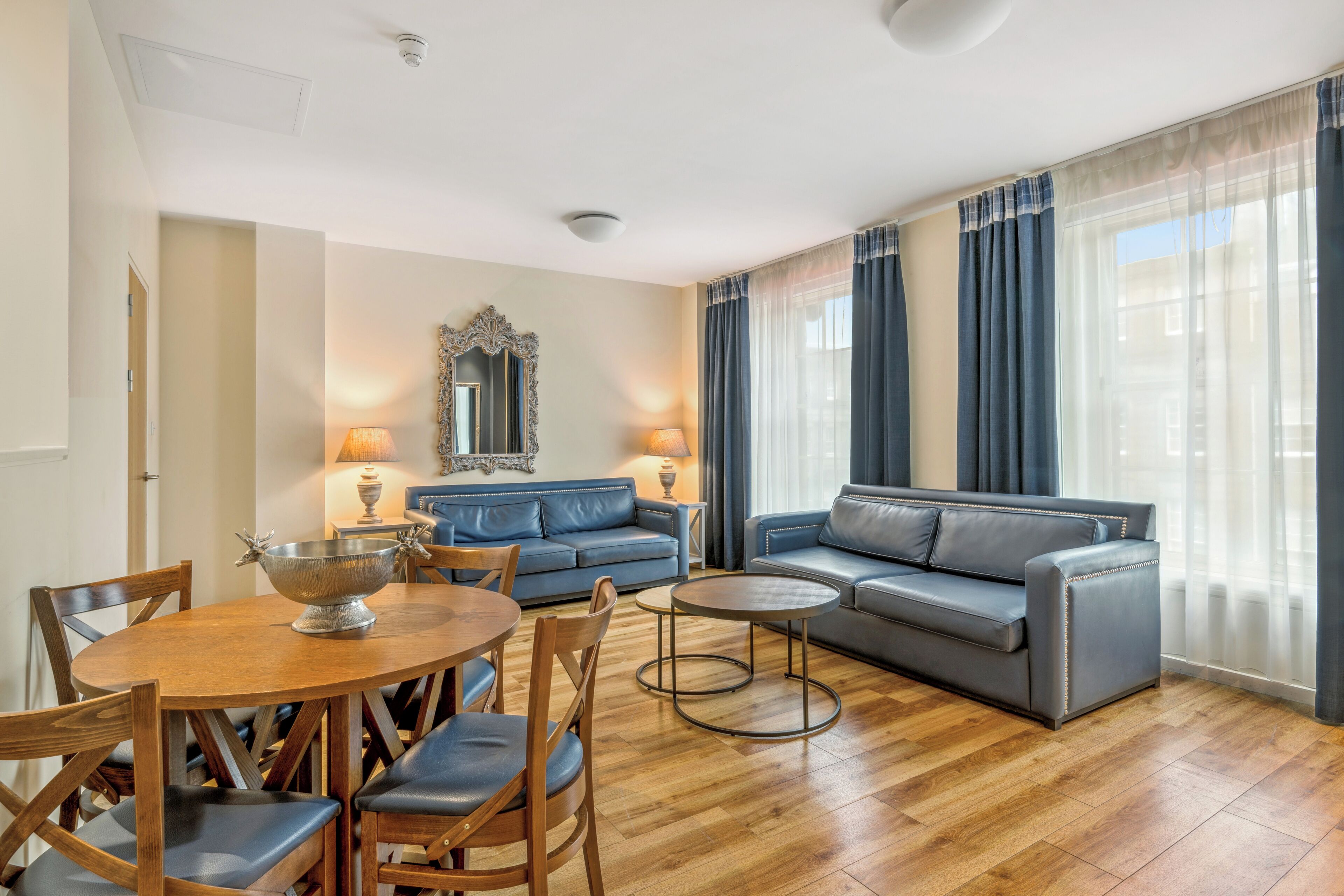 Una sala de estar moderna con comedor, que presenta un sofá azul, una mesa de comedor redonda de madera y un cuenco decorativo con motivos de asta.