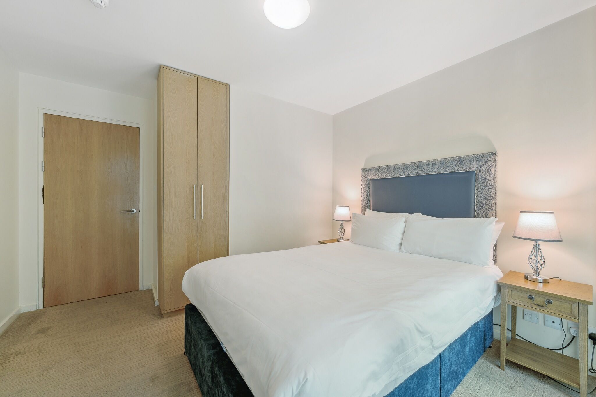 Ein Schlafzimmer mit einem großen Bett, zwei Nachttischen mit Lampen, einem Kleiderschrank und einer Deckenleuchte.