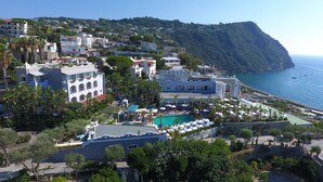 Un complejo turístico en la costa con piscina, varias construcciones y vista al mar.