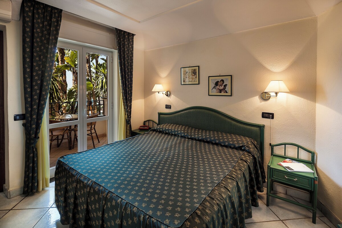 Une chambre à coucher comprenant un lit, une table de chevet, deux lampes fixées au mur et une fenêtre avec des rideaux.