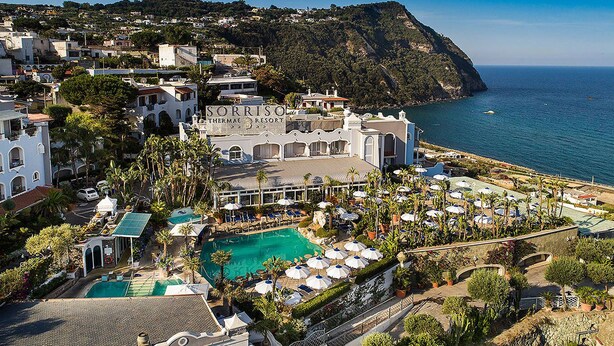 Un resort con una piscina grande, múltiples sombrillas y vistas al mar.