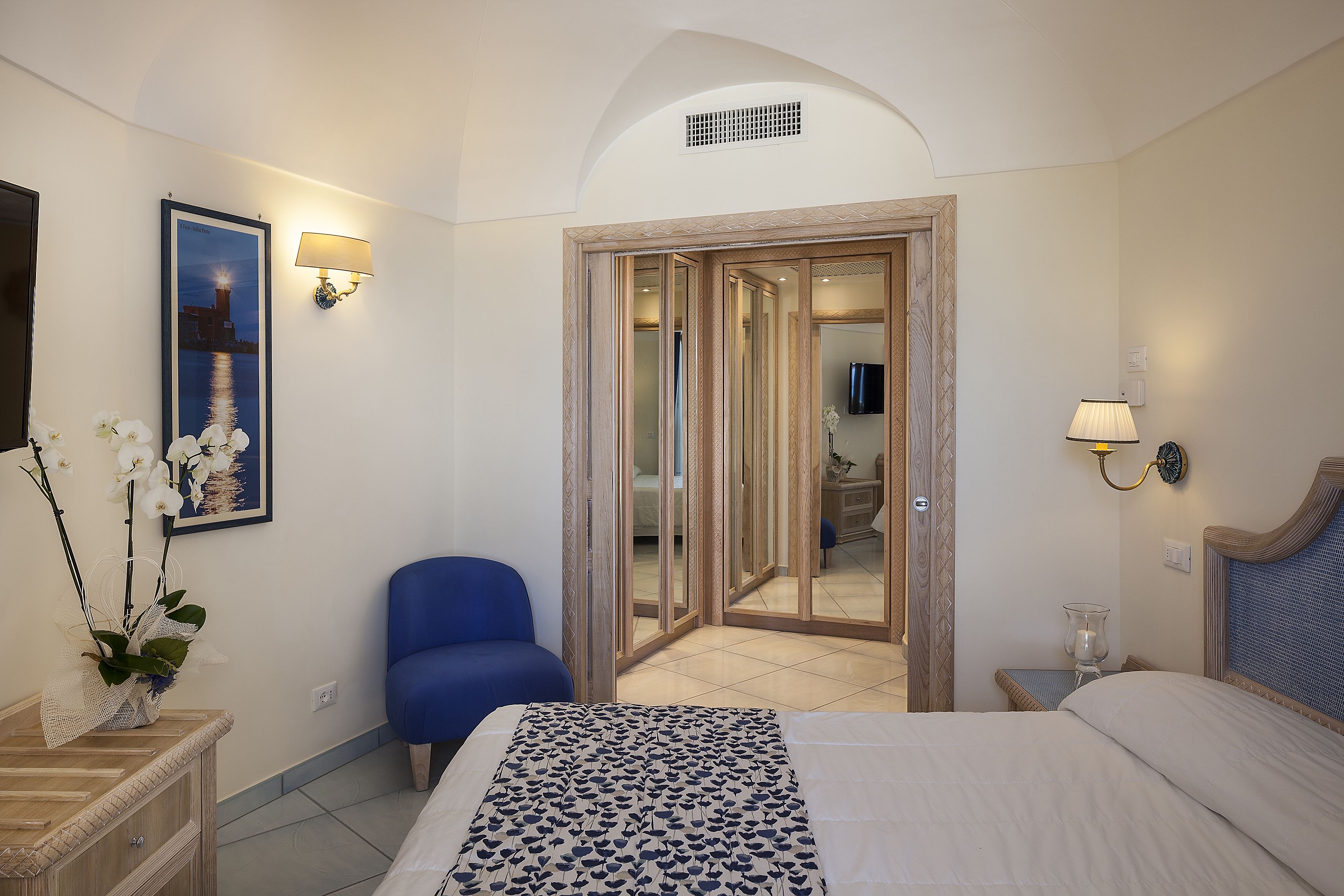 Una camera d'albergo con un letto, una sedia, una scrivania, una lampada, un quadro appeso al muro e una porta che dà su un'altra stanza.