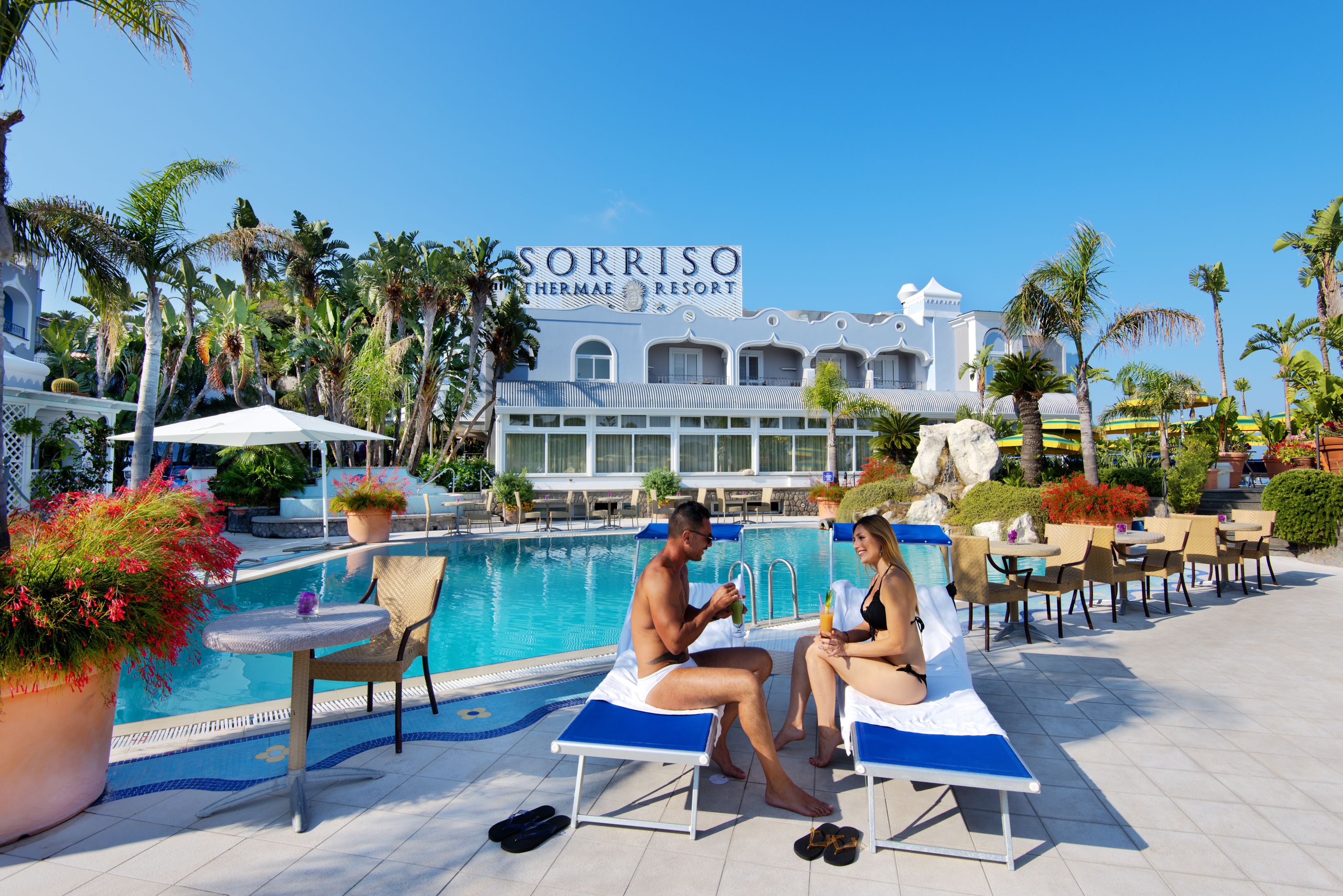 Zona de piscina d'un complex amb gandules, una piscina i un edifici amb la inscripció "Sorriso Thermae Resort".