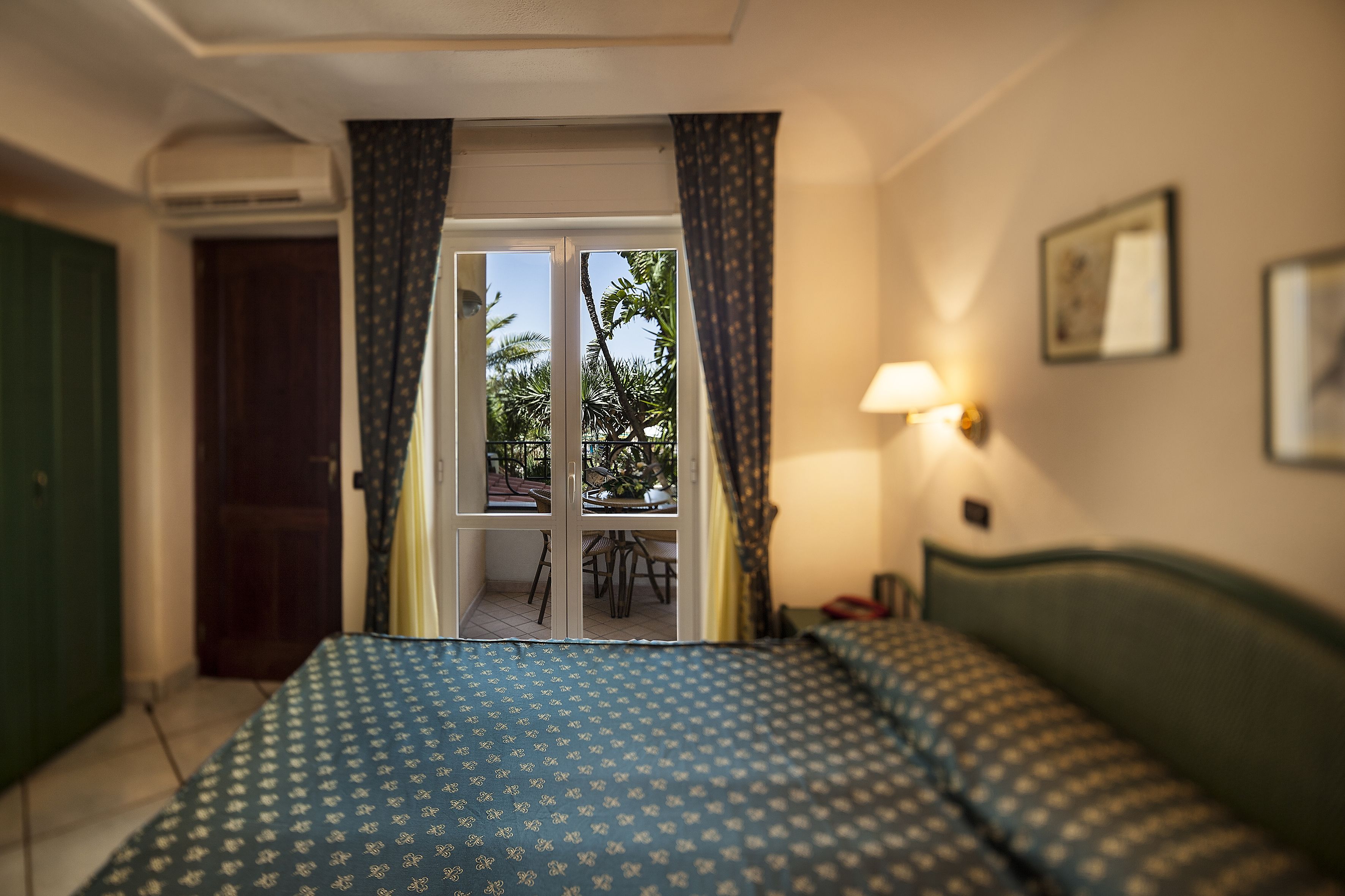 A hotel room with a bed, a desk, a chair, a window with curtains, and a door.