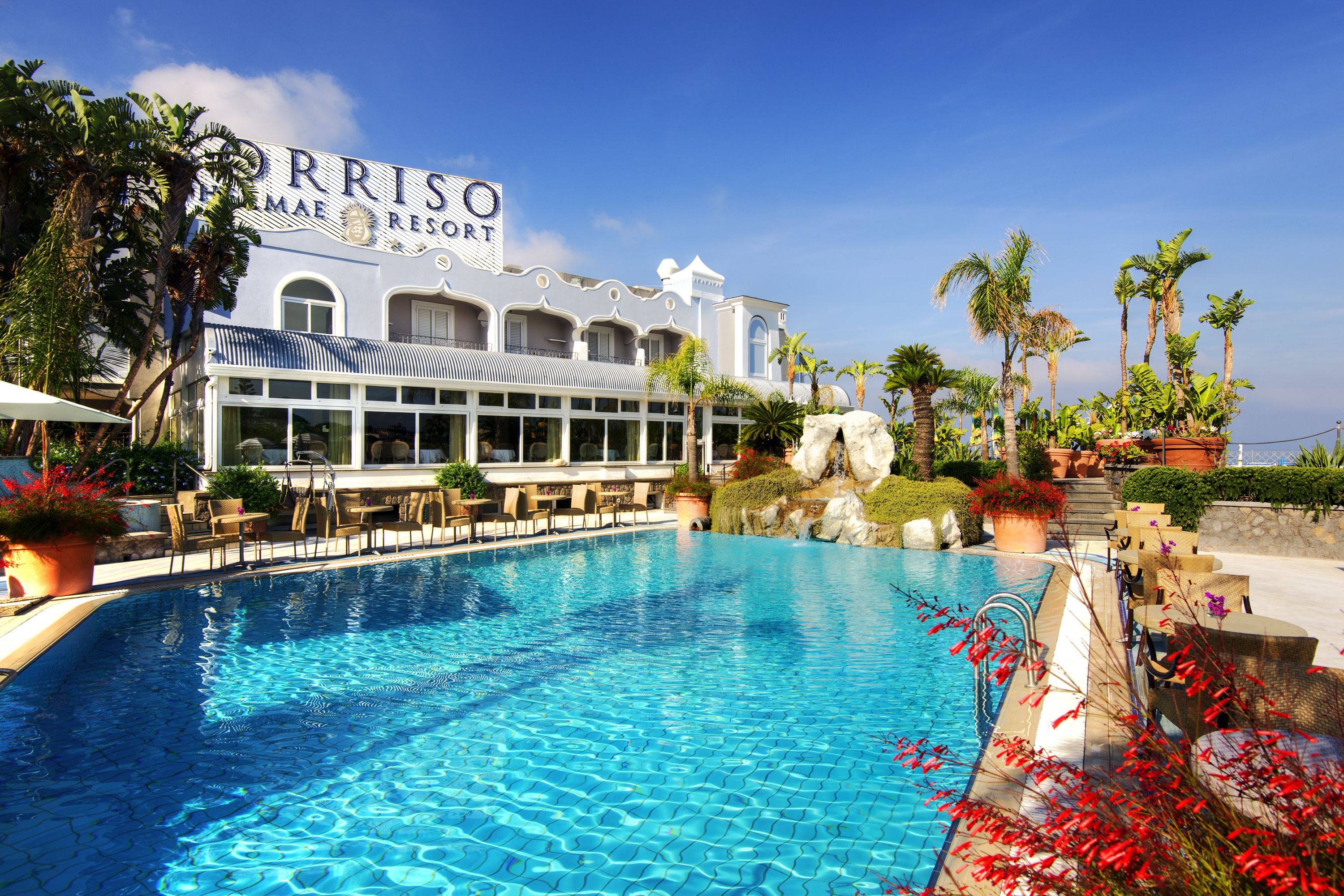 A resort with a pool, palm trees, and a building with 'Perriso' signage.