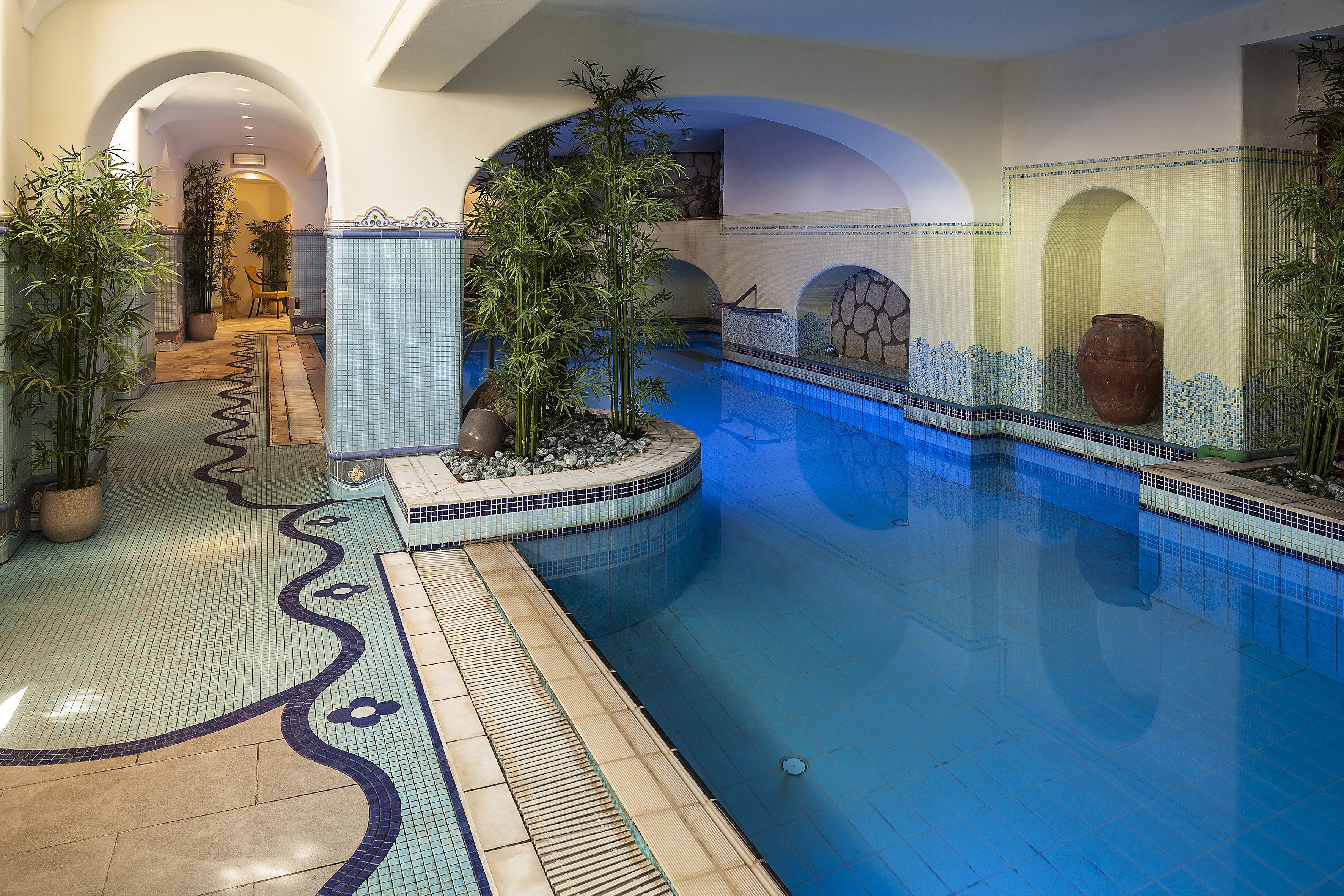 A swimming pool with tiled walls and a tiled floor, surrounded by arches and potted plants.