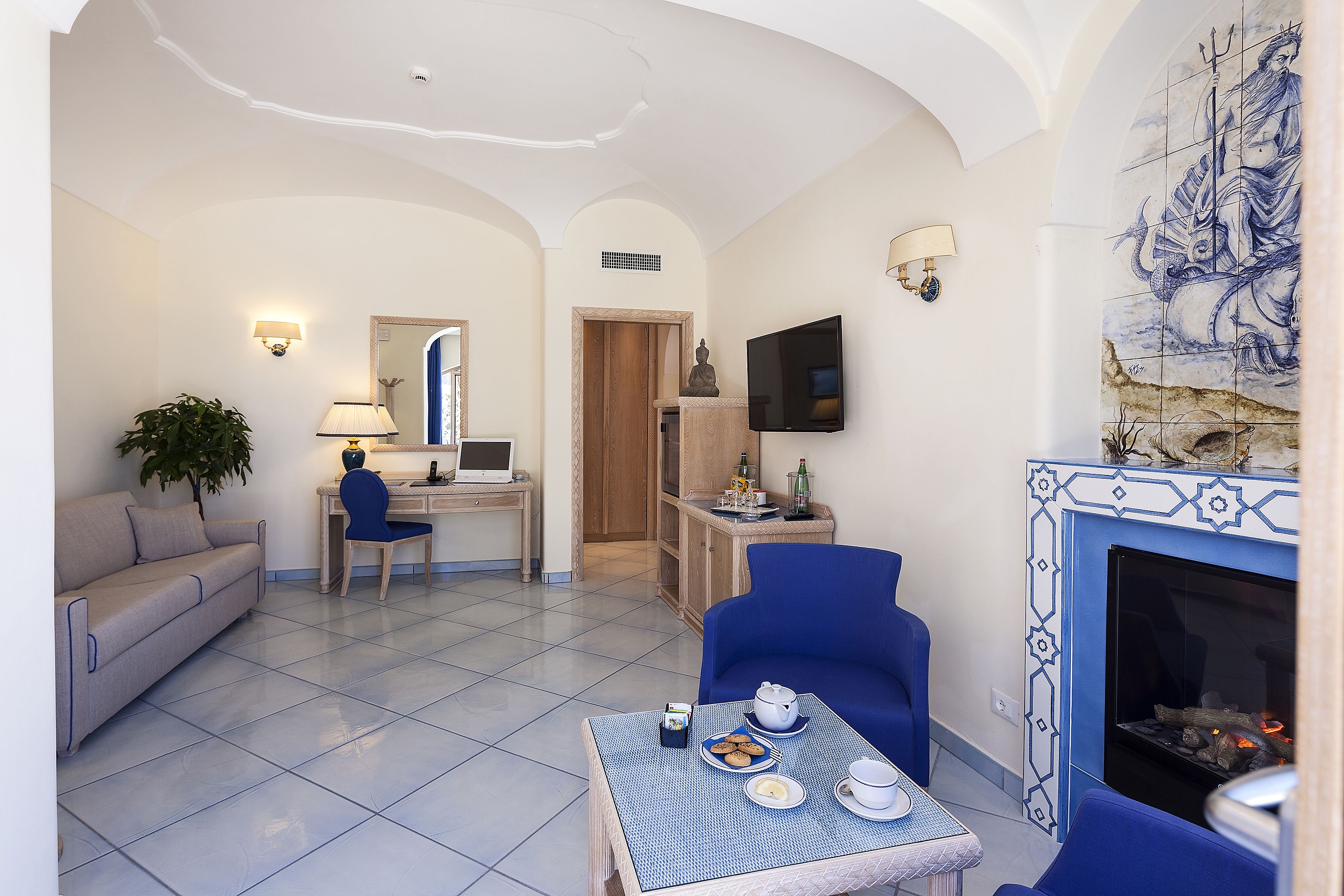 Una sala de estar con un sofá, una mesa de comedor con platos y tazas, un sillón azul, una chimenea y un televisor montado en la pared.