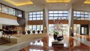 Un vestíbulo amplio con una zona de estar central, ventanas grandes y una escalera que lleva a un nivel superior.
