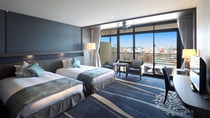 Habitación de hotel con dos camas, un escritorio, una silla y vistas a la ciudad.