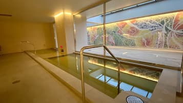 A modern indoor pool area with clear glass walls, a metal handrail, and a colorful abstract mural on the wall.