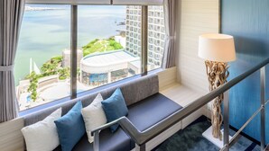 Habitación de hotel moderna con un sofá curvo, vistas al mar y edificios, y una lámpara original.