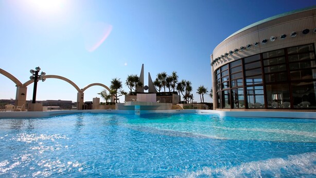 Una piscina con un diseño arquitectónico moderno, que incluye una escultura distintiva y palmeras.