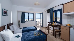 A hotel room with two beds, a dining area, and a kitchen. There is a view of the beach through the windows. - Aegean Sky Hotel & Suites (Hersonissos)