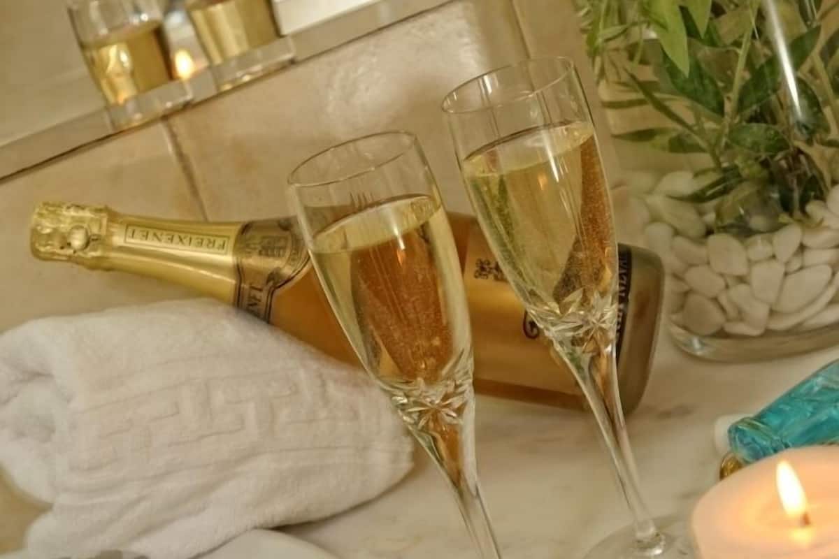 A bathroom with a white sink, two champagne glasses, a bottle of champagne, a towel, and a candle.