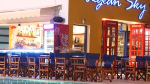 A bar area with a neon sign, poolside seating, and a variety of fruits and snacks on the pool deck. - Aegean Sky Hotel & Suites (Hersonissos)