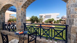 A stone archway leading to a patio with a table and chairs, a blue railing, and a garden with a circular flower bed. - Aegean Sky Hotel & Suites (Hersonissos)