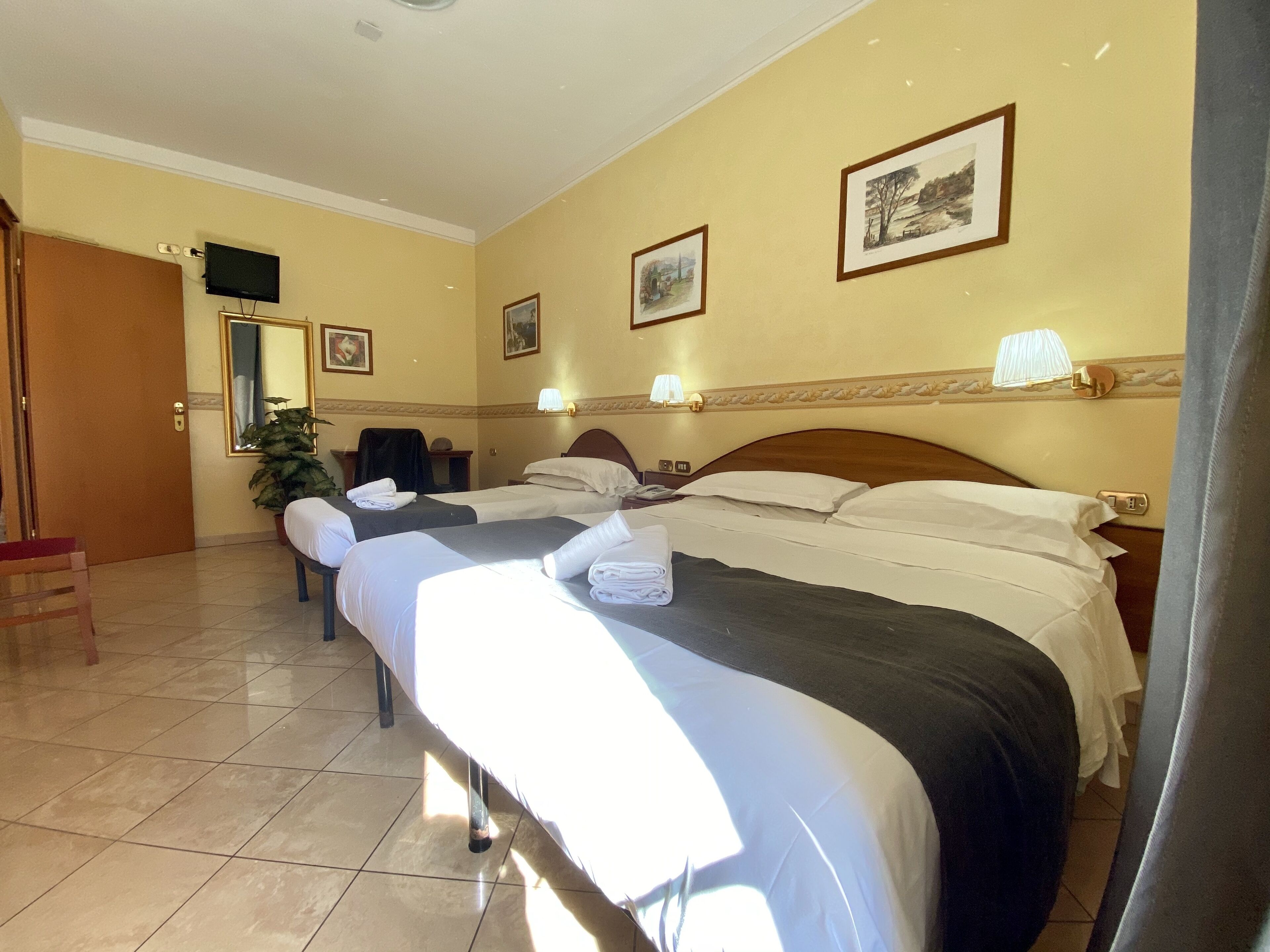 Une chambre d’hôtel avec deux lits, un bureau, une chaise, une télévision et des tableaux encadrés au mur.